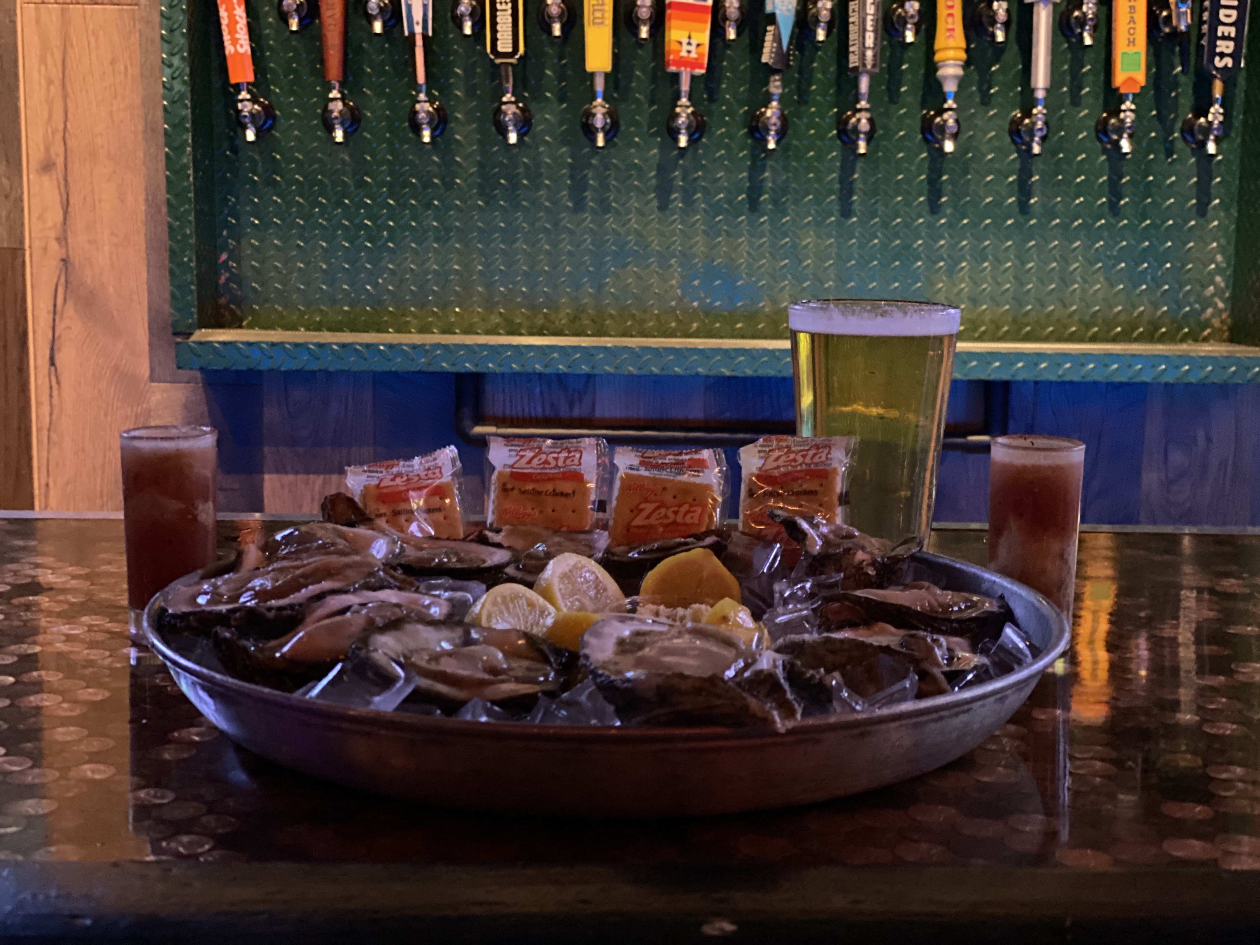 oysters with crackers and a glass of beer with beer taps in the background